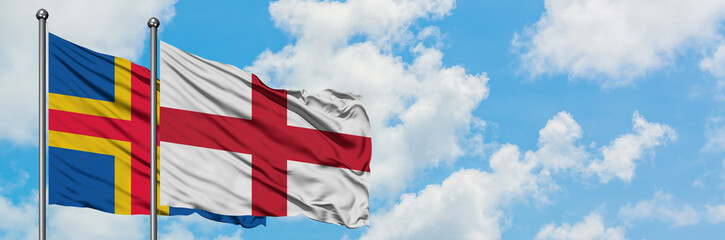 Aland Islands and England flag waving in the wind against white cloudy blue sky together. Diplomacy concept, international relations.