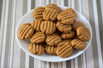 Pile of peanut butter biscuits on white plate, very tasty golden baked sweets, cookies served to eat