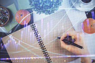 Forex chart hologram on hand taking notes background. Concept of analysis. Double exposure