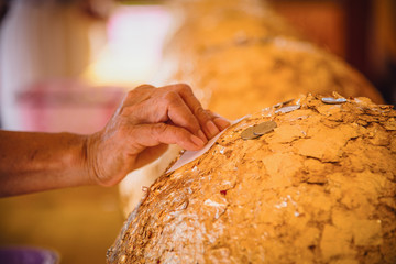 Golden stone carving is a sphere called Loknimit ,some lady hand use gold leaf stick it on for...