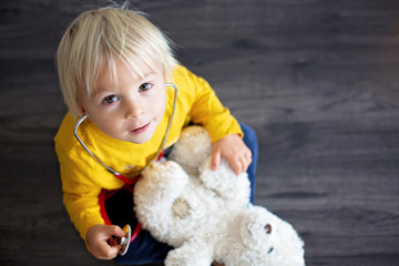 Sweet toddler child, playing doctor, examining teddy bear toy