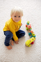 Cute toddler boy, playing with wooden train and teddy bear on isolated background