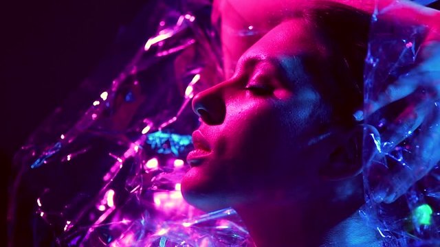 Fashion model woman in colorful bright neon lights posing in studio through transparent film. Beautiful sexy girl in UV. Art design colorful makeup. Slow motion. 4K UHD video footage 3840X2160