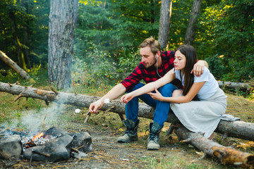 Summer lifestyle. Couple in love having hike picnic nature background. Funny couple eating roasted marshmallows while camping near the lake. Couple in love enjoying picnic in the forest.