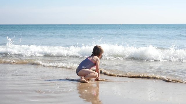 Little Girl Kid sitting close to a Sea Shore, playing with warm Sand - Alicante, Spain