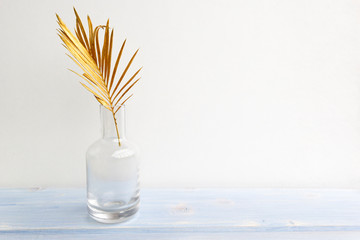 Golden palm leaf in glass vase bottle on light blue wooden background. Creative minimal modern...