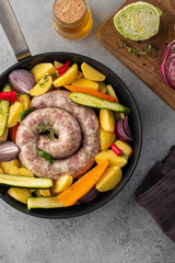 Raw sausages with potatoes, zucchini, carrots and thyme in a grill pan.
