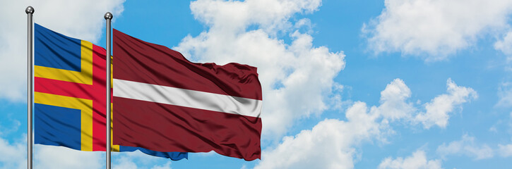 Aland Islands and Latvia flag waving in the wind against white cloudy blue sky together. Diplomacy concept, international relations.