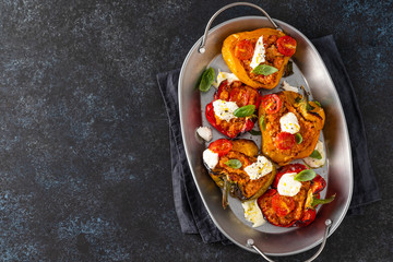 Baked stuffed bell pepper filled with minced meat, onion, tomato, and mozzarella. Dark background. Top view.