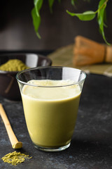 Matcha green tea latte in glass mug with whisk.