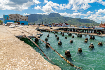 Old rusty ruined caribbean port before reconstruction, demolished dock, collapsed sunk rails, marine customs building, mountain view, Puerto Plata harbor, Dominican Republic