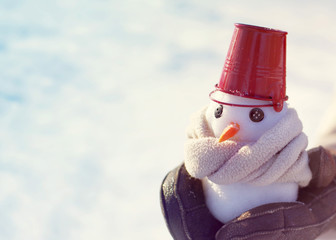 Little cute snowman in a scarf in his hands on a sunny winter day. Christmas card