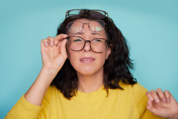 frames trying many eyeglasses. girl holding glasses standing on turquoise background, Concept: poor...
