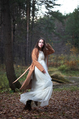 girl in a white dress and a brown coat in the autumn forest