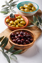 Different types of olives green and black in bowls on white table.