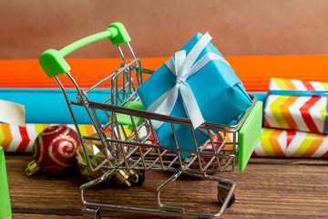 Gift boxes in shopping cart and colorful wrapping paper on a wooden brown background. The concept...