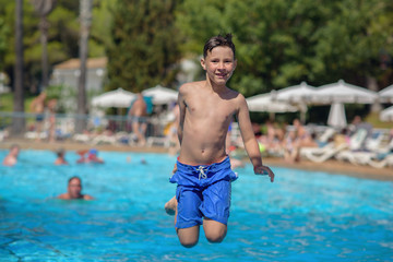 Boy having fun on summer vacation. He is making high jump into swimming pool.