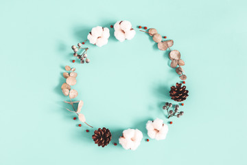 Winter composition. Wreath made of dried leaves, cotton flowers, berries, pine cones on blue background. Autumn, fall, winter, christmas concept. Flat lay, top view, copy space