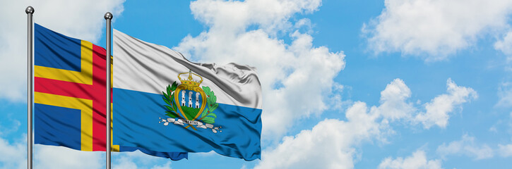 Aland Islands and San Marino flag waving in the wind against white cloudy blue sky together....