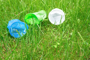 Bright colourful disposable plastic cups isolated on green grass. Ecology problem. Copy space. Top view.
