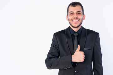 Portrait of happy young bearded Persian businessman in suit giving thumbs up