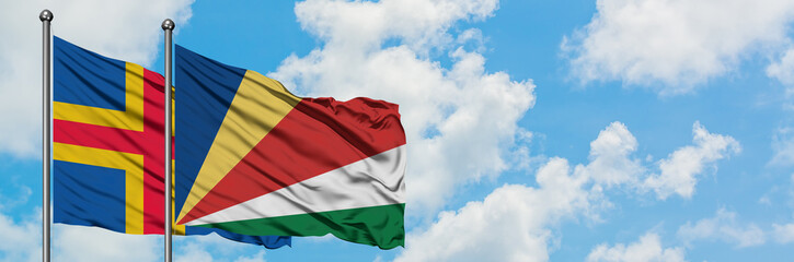 Aland Islands and Seychelles flag waving in the wind against white cloudy blue sky together. Diplomacy concept, international relations.