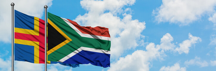 Aland Islands and South Africa flag waving in the wind against white cloudy blue sky together. Diplomacy concept, international relations.