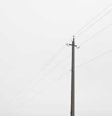 The electric pole and wires in front of gray foggy cloud. Concept of minimalist photo