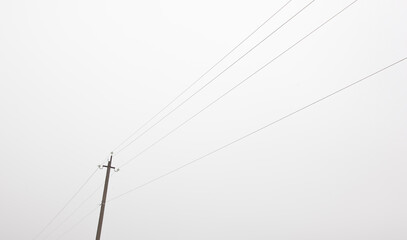 The electric pole and wires in front of gray foggy cloud. Concept of minimalist photo