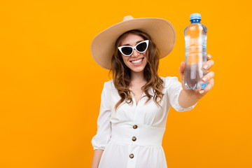 stylish brown-haired woman with a smile on a yellow background, holding a water bottle in her...