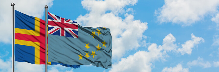 Aland Islands and Tuvalu flag waving in the wind against white cloudy blue sky together. Diplomacy...