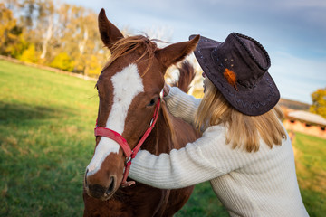 Obraz premium Woman with cowboy hat is hugging her young horse at pasture