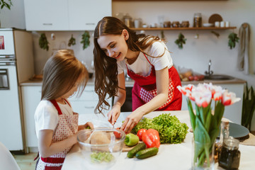 young mother teaches daughter to set the table. Kitchen, vegetables on the table and flowers