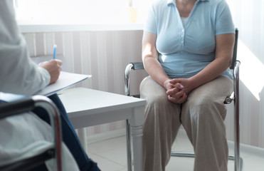 An elderly woman sits at a doctor's appointment. A gynecologist consults a patient in a clinic office.