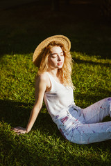 a young student in jeans, a T-shirt and a hat sat down on the grass and set her face to the sun. she is resting