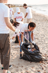 Image of people volunteers cleaning beach from plastic with trash bags