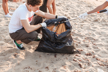 Image of volunteers guys cleaning beach from plastic with trash bags