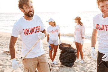 Photo of smiling volunteers cleaning beach from plastic with trash bags