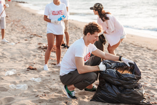 Image of teenage volunteers cleaning beach from plastic with trash bags