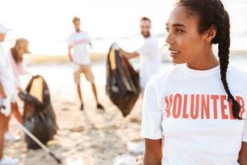 Photo of pleased female volunteer cleaning beach from plastic