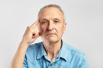Elderly man points finger at his head on white background. Senile diseases, dementia, Alzheimer's,...