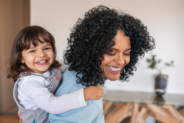 Laughing mother piggybacking her cute daughter around the house
