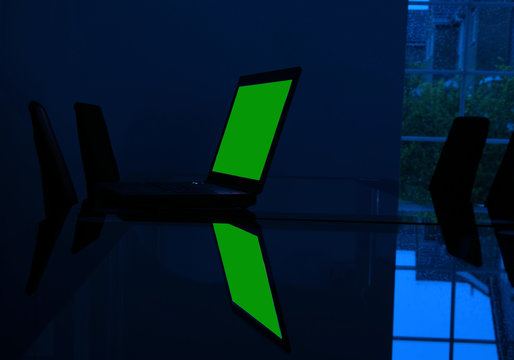 Laptop Computer On Glass Desk In Empty Dark Room With Rain Spattered Window And Green Screen For Own Copy Or Graphic