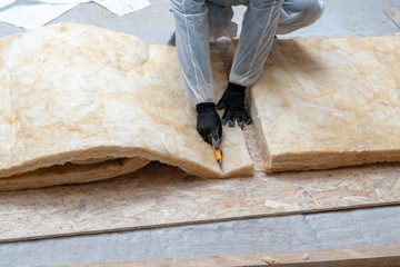 Professional worker man installing thermal insulation rock wool under the roof