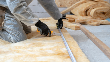 Professional workman installing thermal insulation rock wool under the roof - obrazy, fototapety, plakaty