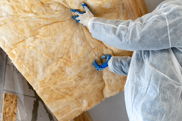 Professional workman installing thermal insulation rock wool under the roof