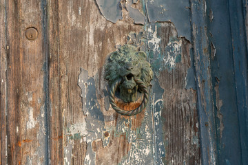Old wooden door with peeled paint and lion shaped handle. Texture of wood and paint. Background photo with space for text. Travel photo. Venice. Italy.