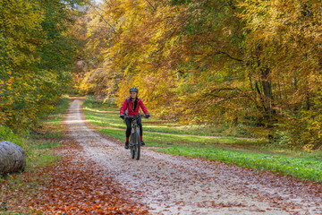 nice senior woman riding her electric mountain bike in a colorful autumn forest of the swabian Alb, Baden Wuerttemberg,Germany