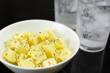 Mozzarella cheese cubes in a white bowl in a black table with two cups of sparkling water in the background