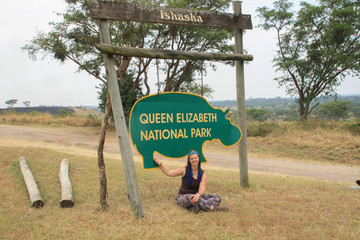 Young woman tourist sitting under the sign of Queen Elizabeth National Park in Uganda.